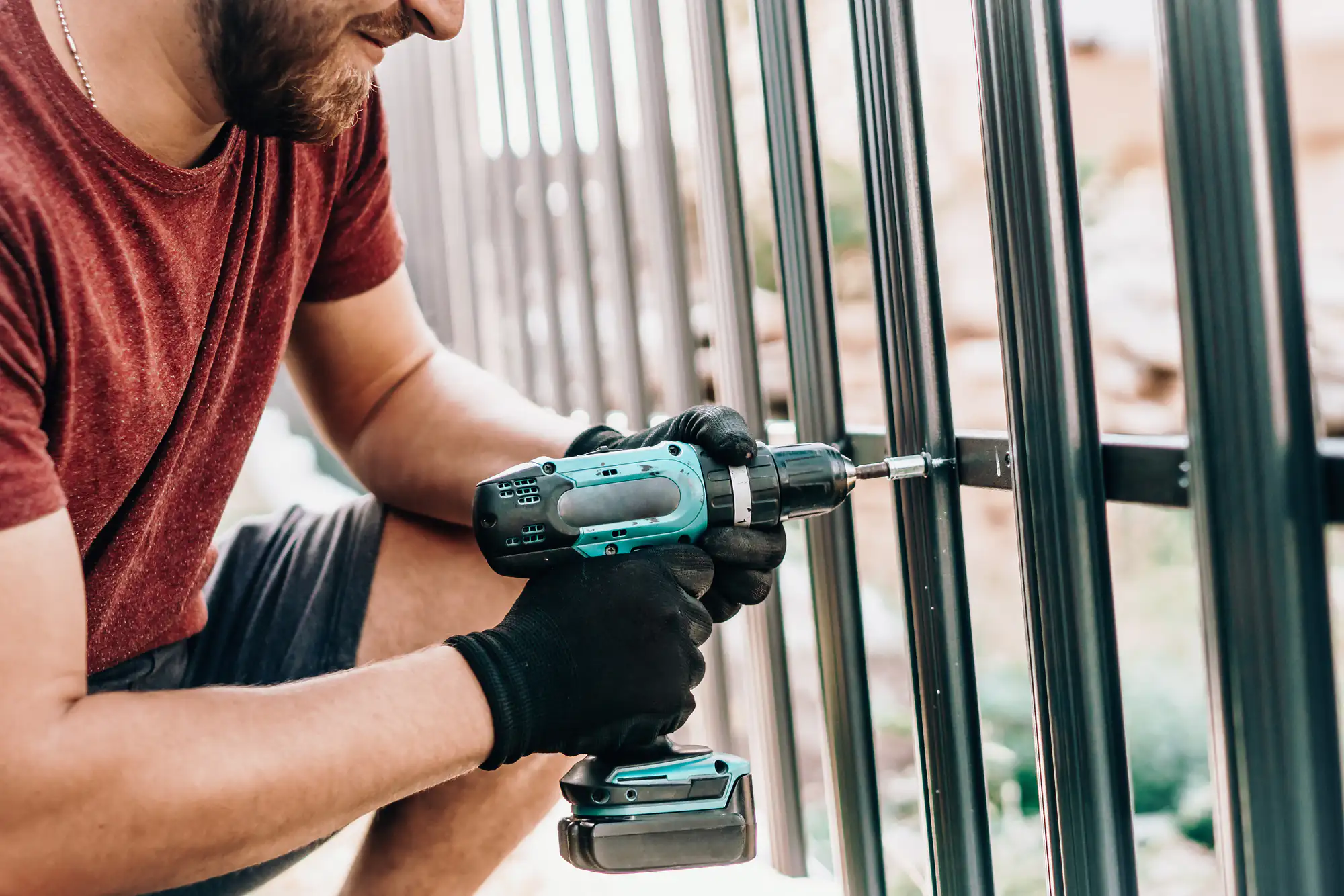 A fence contractor in Suffolk County, NY, wearing a red shirt, uses a cordless drill on site.