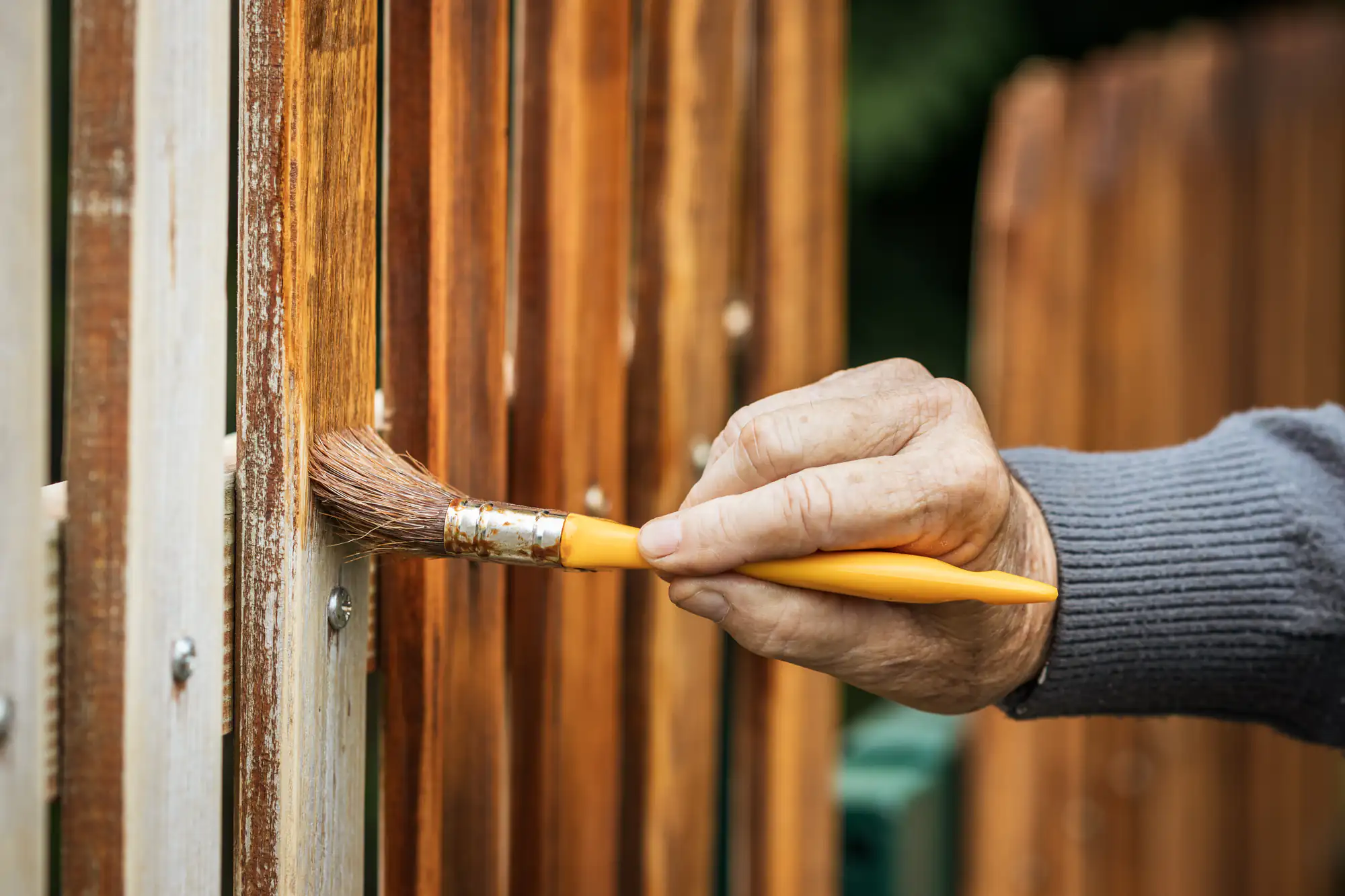 A skilled fence contractor in Suffolk County, NY, paints a wooden fence with expert precision.